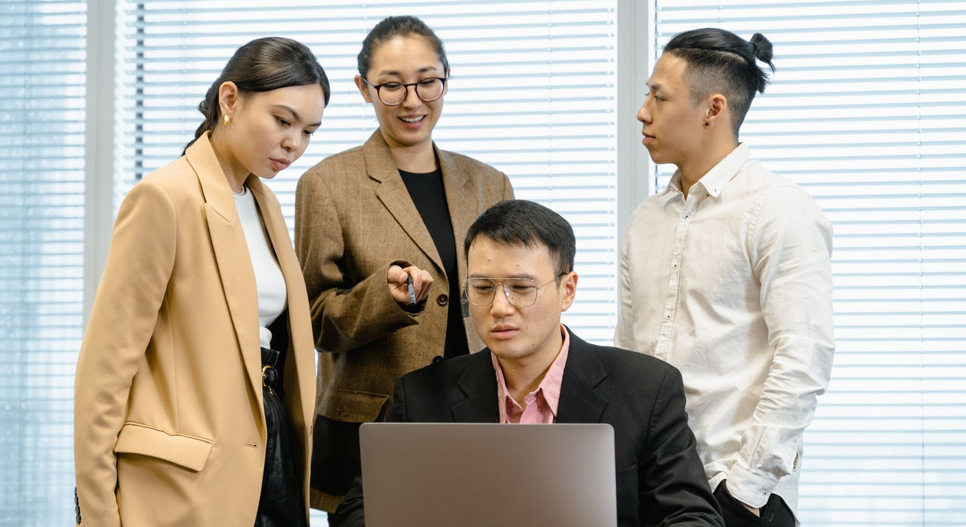 Four colleagues discussing work around a laptop in an office.